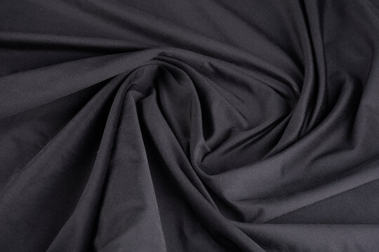 Close-up top-down view of shiny black dry-fit fabric with a twisted, folded polyamide texture.