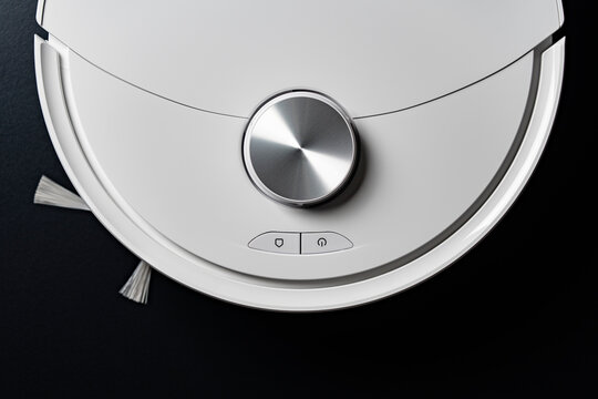Top view of modern white robotic vacuum cleaner on dark background, closeup. Minimalist overhead shot of smart robot vacuum cleaner highlighting metal sensor and control buttons on sleek black floor