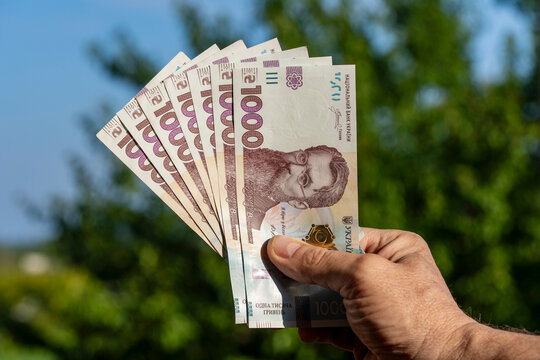 Man holding fan of Ukrainian one thousand hryvnia banknotes outdoors. Closeup of hand with Ukrainian national currency bills of 1000 UAH on blurry green nature background