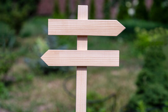 Blank wooden directional signpost with arrows pointing left and right in garden. An empty wooden sign with two opposite arrows on blurry green nature background ready for custom text or message