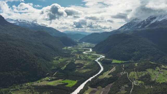 Aerial perspective of the meandering Futaleufu River flowing through a lush green valley surrounded by snow-capped mountains in Patagonia, Chile.