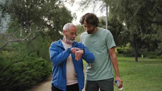 Senior man and his son jogging doing sport together, tracking cardio fitness levels using smartwatch app 