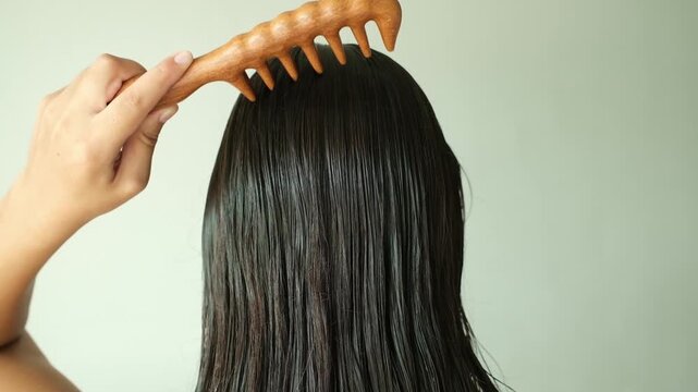 Natural Wooden Comb for Healthy Hair Care. Back view of a brunette woman slowly combing freshly washed hair with a natural wooden comb.