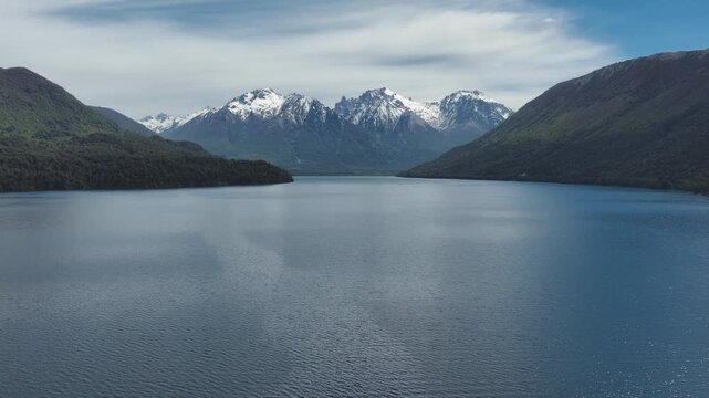 Scenic landscape featuring a wide view of snow-capped mountains reflecting on the calm, deep blue water of a vast lake