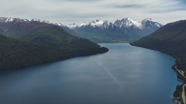 Aerial drone view of the deep blue waters of Mascardi Lake surrounded by lush forests and dramatic snow-capped mountain peaks in Patagonia, Argentina.