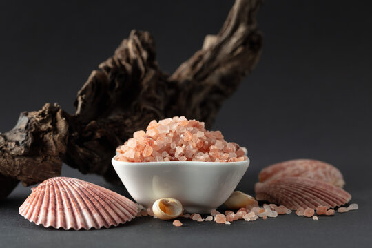 Pink himalayan salt with snags and seashells on a black background.