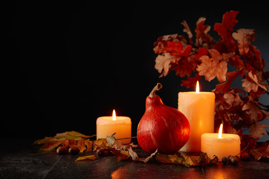Still life with pumpkin, dried-up leaves, and burning candles.