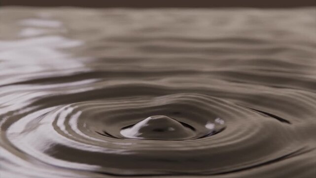 Falling primary droplet striking sepia pool in shallow tray, creating crown and ringed ripples
