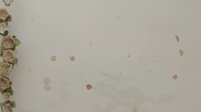 Drifting rose petals falling from top and settling on cream backdrop near garland, copy space