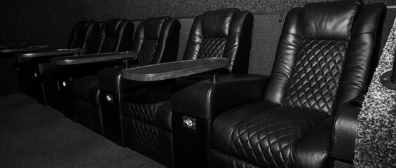 Obraz premium Luxury black and white VIP cinema seats with leather recliners and wooden trays. Premium theater interior for private screening. Elegant monochrome furniture
