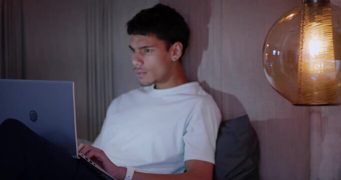 African American man responding to laptop, typing and adjusting eyeglasses while studying at home