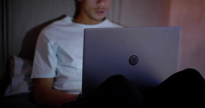 African American man in twenties on bed with laptop, lifting head, reacting to surprising message