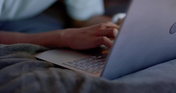 African American man typing, leaning forward and reading notification on silver laptop on couch