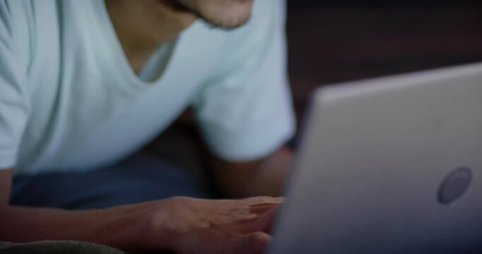 African American man in T-shirt reclining on blanket at home hand resting focusing typing on laptop