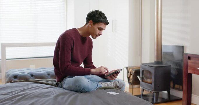 African American man in maroon sweater tapping tablet on bed, picking up card, tapping for payment