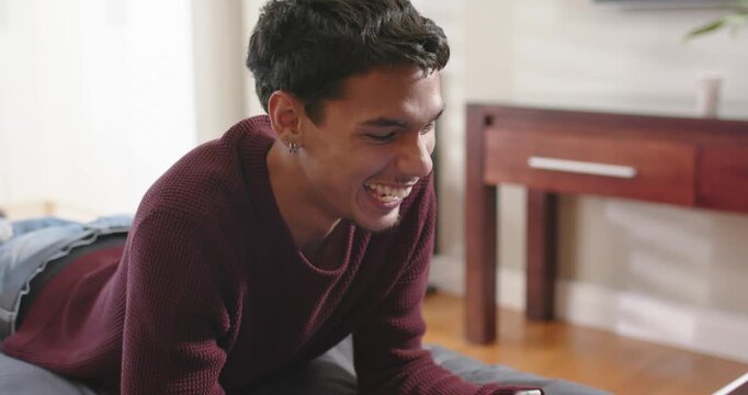 African American man in burgundy sweater lying on bed using laptop, seeing message, smiling, typing