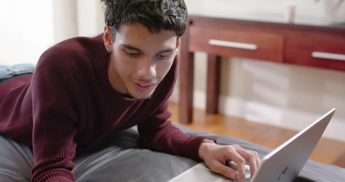 African American man wearing sweater typing on silver laptop on bed holding card entering payment