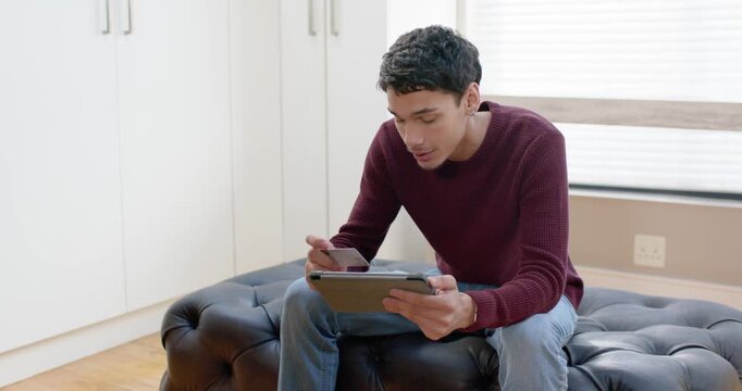 African American man glancing right shifting on ottoman at home using stylus on tablet studying
