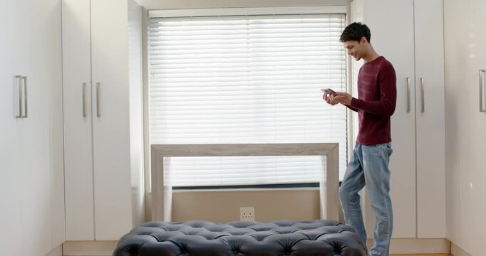 Adult man standing right of frame by wardrobe, using smartphone and checking messages, copy space
