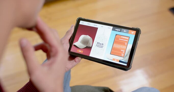 African American man viewing Black Friday banner holding tablet and inspecting cap page at home