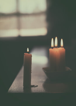 Close-up of four lit candles on a table with a window in the background