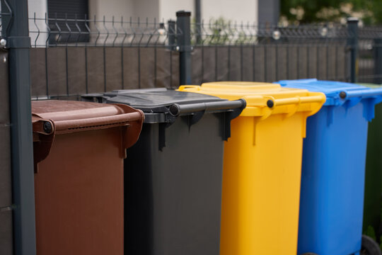 Colorful recycling and waste bins standing in a row beside fence in residential neighbourhood