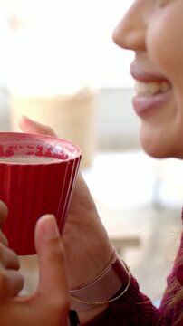 Vertical video: Smiling woman wearing maroon scarf on cue at cafe lifting red cup showing watch