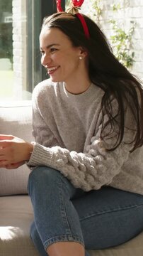 Vertical video: Handing cup lady wearing knit sweater jeans and red antlers as pal entering on sofa