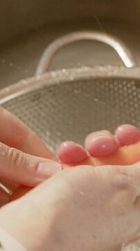 Vertical video: Rinsing carrot with hands as tap runs at kitchen sink to clean, colander, wristband