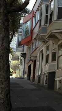 Vertical video: Tilting handheld camera up steep urban street to reveal orange bay window and tree
