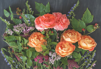 Garden bouquet with coral and orange English roses, yarrow, wildflowers and raspberry branches on dark background © kulikovan