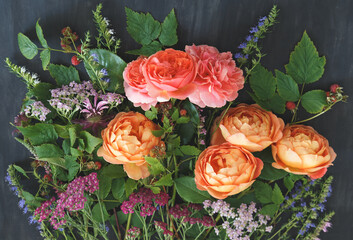 Garden bouquet with coral and orange English roses, yarrow, wildflowers and raspberry branches on dark background © kulikovan