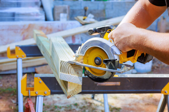 Worker uses circular saw to cut wood on workbench outdoors