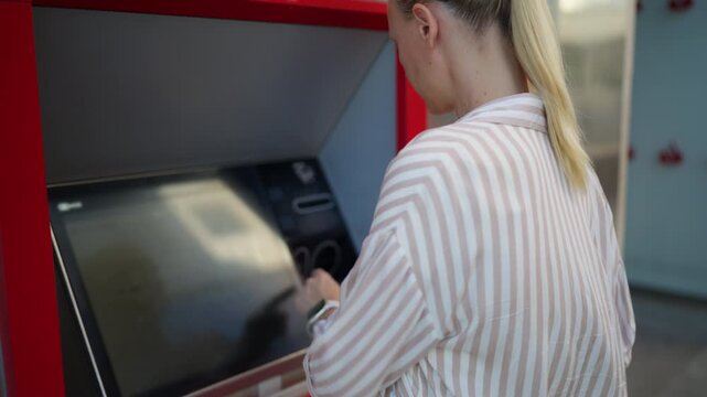 Blonde woman using ATM machine for everyday banking transaction. Secure cash withdrawal, personal finance, banking services and modern financial technology concept.
