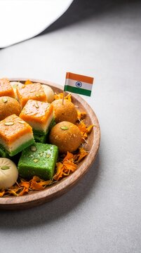 Traditional Indian sweets platter decorated with marigold petals and miniature national flag for Independence Day celebration on wooden plate