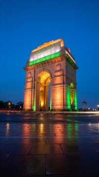 Majestic stone triumphal arch monument illuminated with vibrant green and orange lights against a deep blue evening sky in a capital city urban plaza