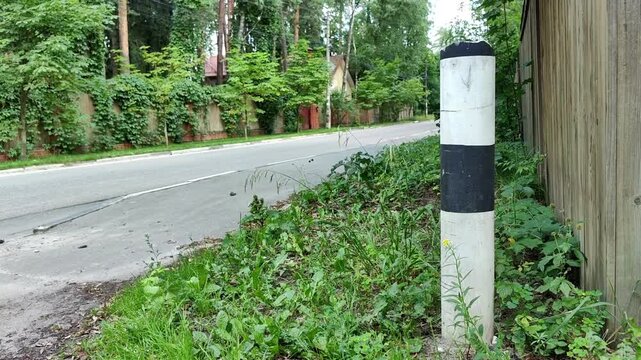 Black and white roadside delineator post beside a quiet street, traffic infrastructure, road safety, transport guidance, suburban travel.