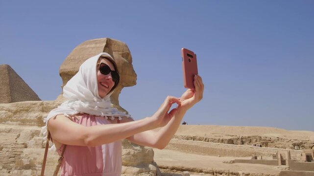 Smiling female traveler taking a selfie with the Great Sphinx of Giza in Egypt, capturing unforgettable travel memories at one of the world's most iconic ancient landmarks.