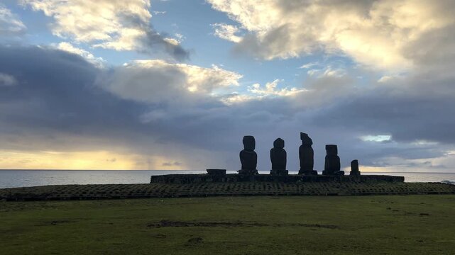  Ahu Tahai ceremonial complex on Easter Island, Chile. Historic Moai statues overlooking the Pacific Ocean on the sunset with scattered clouds.