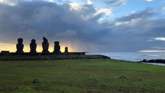  Ahu Tahai ceremonial complex on Easter Island, Chile. Historic Moai statues overlooking the Pacific Ocean on the sunset with scattered clouds.