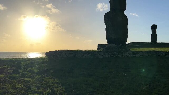  Ahu Tahai ceremonial complex on Easter Island, Chile. Historic Moai statues overlooking the Pacific Ocean on the sunset with scattered clouds.