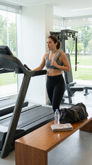Fototapeta premium Fit woman jogging on treadmill in bright gym with towel and gear