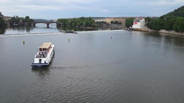Tracking shot of tour boat cruising along river under city bridges on overcast day. Riverboat on the Vltava in Prague