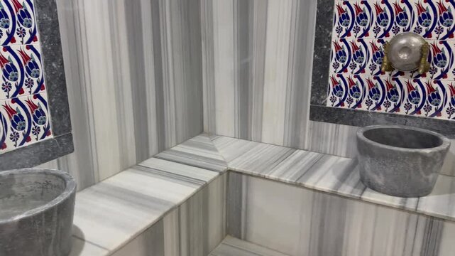 Traditional marble kurna wash basin with water inside an authentic Turkish bath hamam. Beautiful brass water taps are mounted on a wall decorated with handmade Iznik ceramic tiles with floral patterns