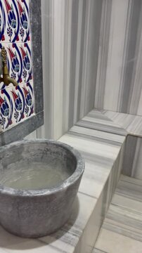 Traditional marble kurna wash basin with water inside an authentic Turkish bath hamam. Beautiful brass water taps are mounted on a wall decorated with handmade Iznik ceramic tiles with floral patterns