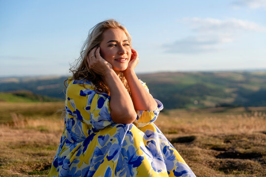 Woman enjoys sunny weather on a hillside surrounded by green fields at golden hour