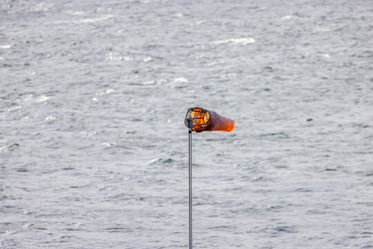 Orange Windsock On Pole Over Gray Water At Tsawwassen Coastline Indicating Wind Direction And Safety
