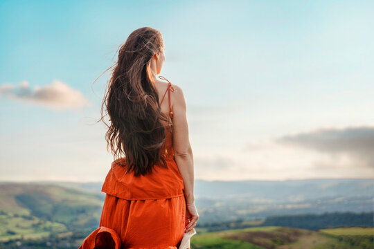 Woman stands on a hilltop looking at the landscape during a sunny day in the countryside