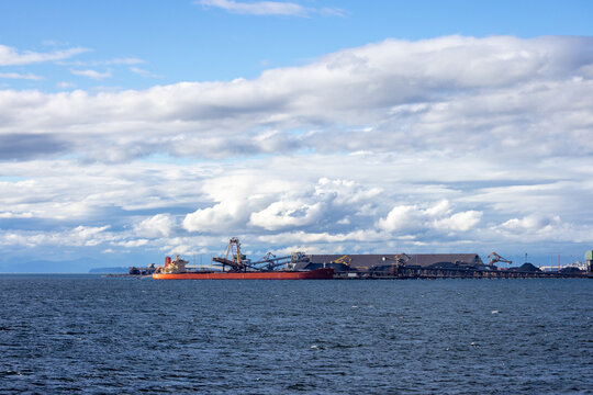 Orange Bulk Carrier Docked At Industrial Coal Terminal In Tsawwassen, British Columbia, Canada Under Cloudy Sky