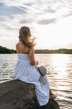 Woman sitting on a rock by the water during sunset 